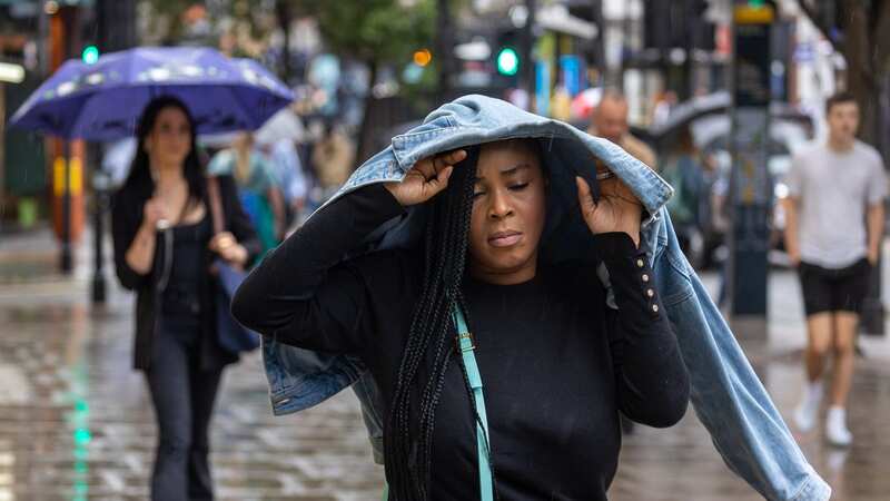 A woman hides from the rain under her jacket in a drizzly central London (Image: Marcin Nowak/LNP)