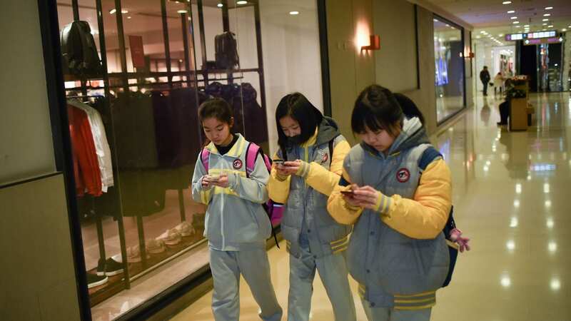 A group of Chinese teens walk through a mall while looking at their smartphones in Beijing (Image: AFP via Getty Images)