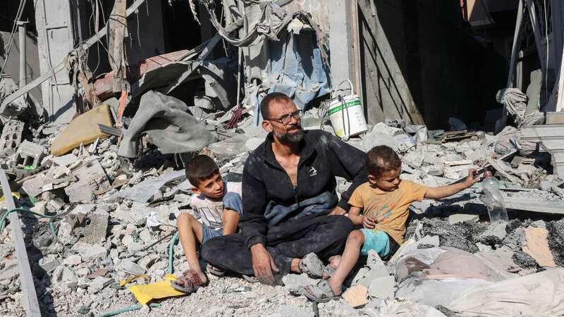 A Palestinian man sits with members of his family outside a building destroyed in an Israeli air strike in Rafah in the southern Gaza Strip (Image: AFP via Getty Images)