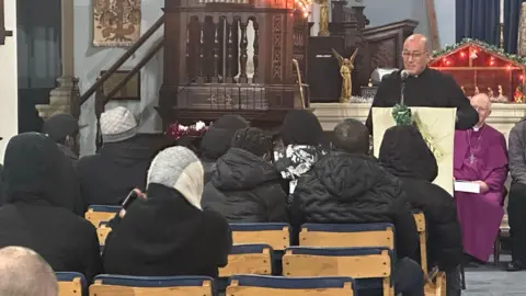 Rev Jesse van der Val speaks to people gathered in the church