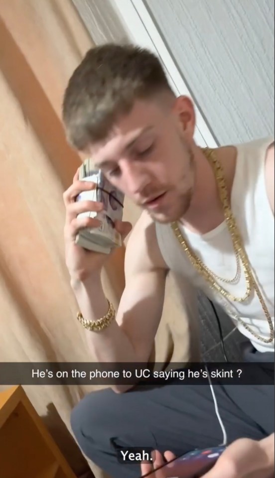A man wearing gold chains holds a stack of cash to his ear while speaking on the phone, claiming to be struggling financially. dqxikeidqkikdinv