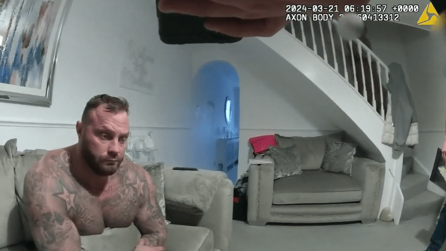 Screenshot of a shirtless tattooed man sitting on a couch in a living room. dqxikeidqkikdinv