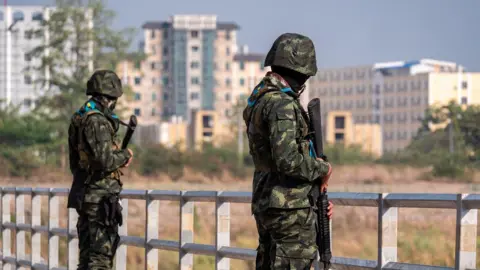 Jonathan Head/BBC Tall buildings in Myanmar&rsquo;s Myawaddy seen from Thailand&rsquo;s border, where armed guards stand on a bridge   dqxikeidqkikdinv