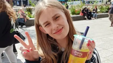 Family handout Rhianan Rudd holding up a bubble tea and giving a peace sign to the camera dqxikeidqkikdinv