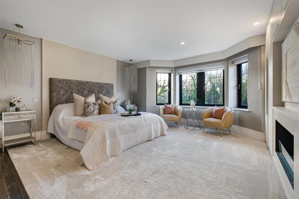 A bedroom with a large window and white curtains, a bed with a neutral-toned headboard and bedding, and two abstract art pieces above the bed.